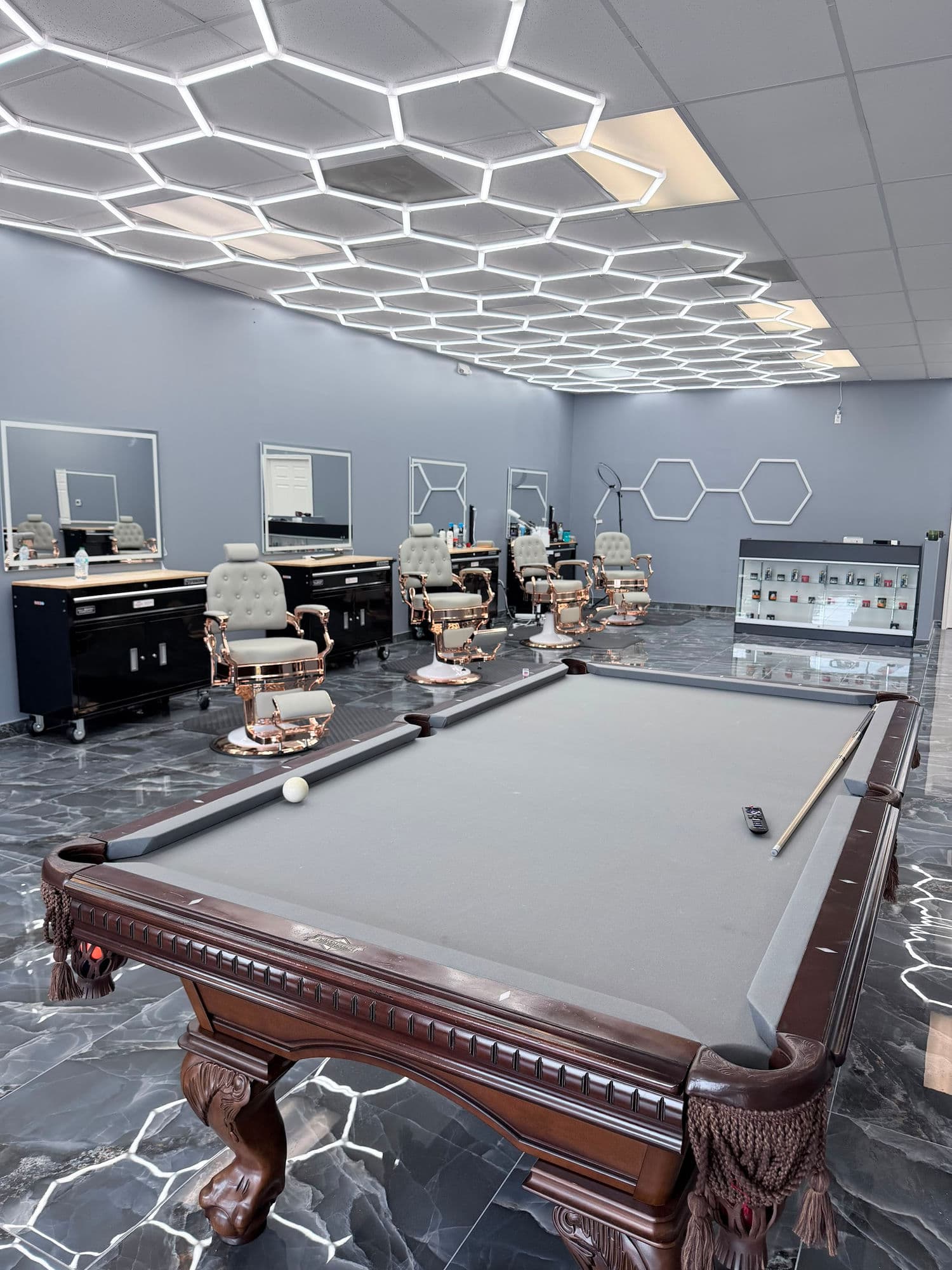 Inside Benja Barber Shop in Humble — rose gold barber chairs, marble floors, and a pool table under hexagon lighting
